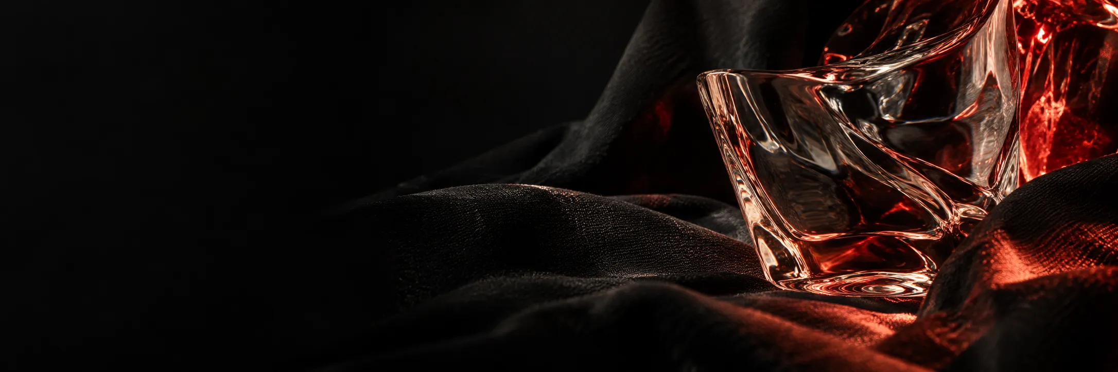 A sculptural glass object reflecting red light against flowing black fabric